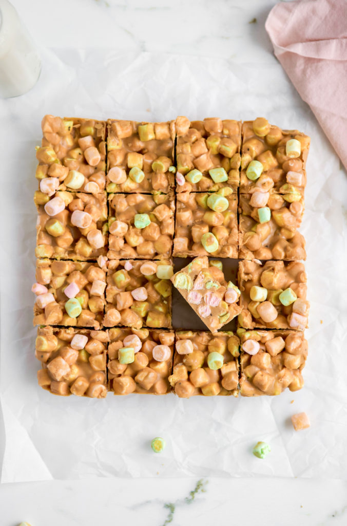 Easy no bake peanut butter marshmallow square recipe on parchment paper with pink napkin off to the side.