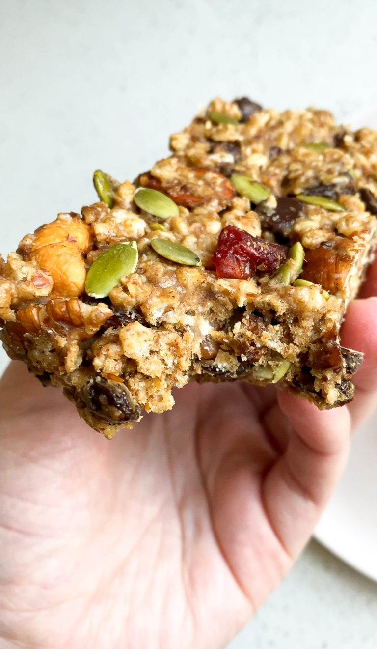 Side angle of hand holding a gluten-free vegan protein bar with nuts and seeds.