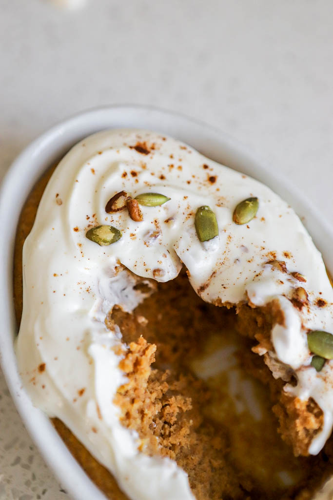 a half-eaten casserole dish with pumpkin pie baked oats topped with Greek yogurt frosting, nuts and seeds