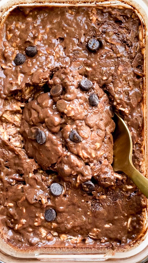 a golden spoon being inserted in a casserole dish with chocolate peanut butter overnight oats 