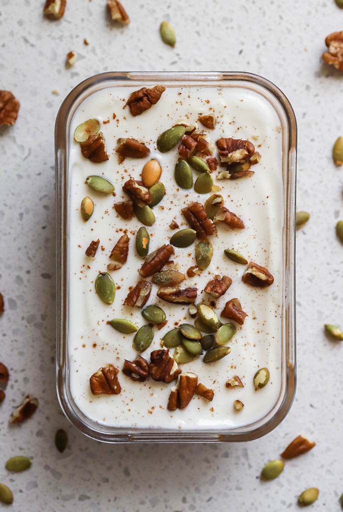 overhead shot of pumpkin overnight oats in a glass container topped with nuts and seeds