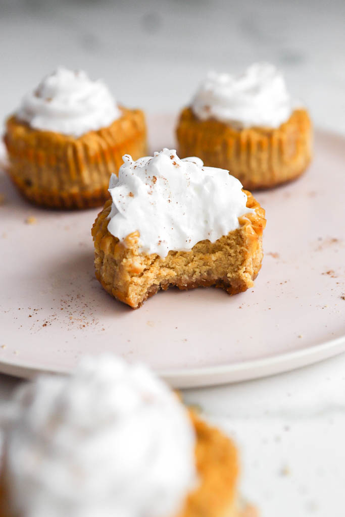 bite shot of a mini pumpkin pie cheesecake with whipped cream on a pink serving plate