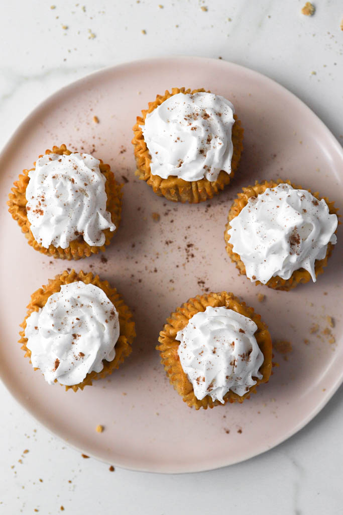 top down shot of mini pumpkin cheesecake bites with whipped cream and pumpkin pie spice sprinkled on top