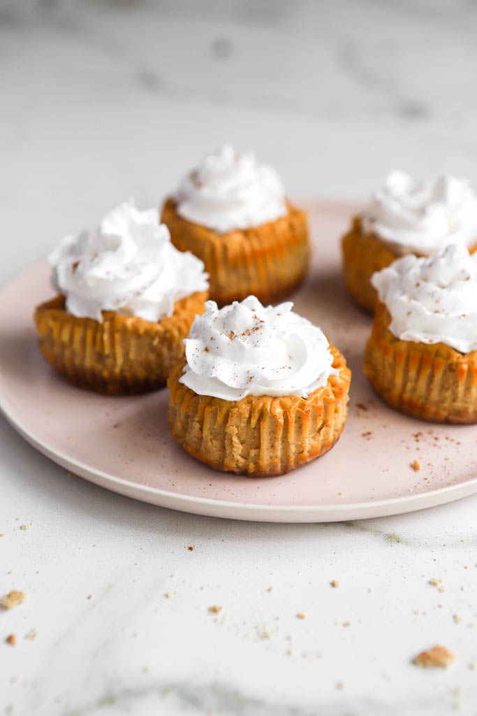 5 mini pumpkin pie cheesecake bites with cool whip on a pink serving plate