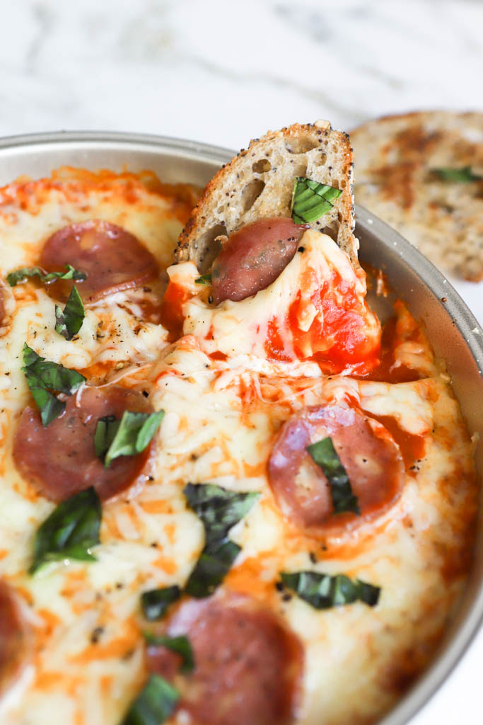 close up shot of pepperoni pizza dip with cream cheese and basil leaves with sourdough