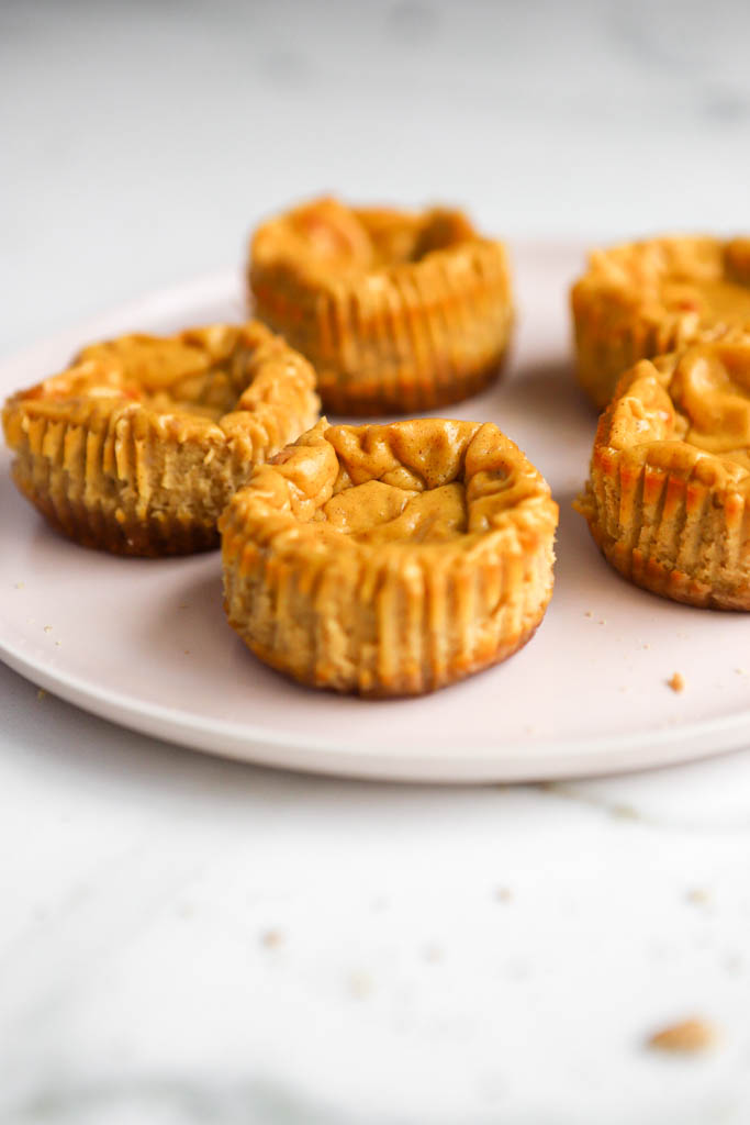 side view of mini pumpkin pie cheesecakes on a pink plate and white background