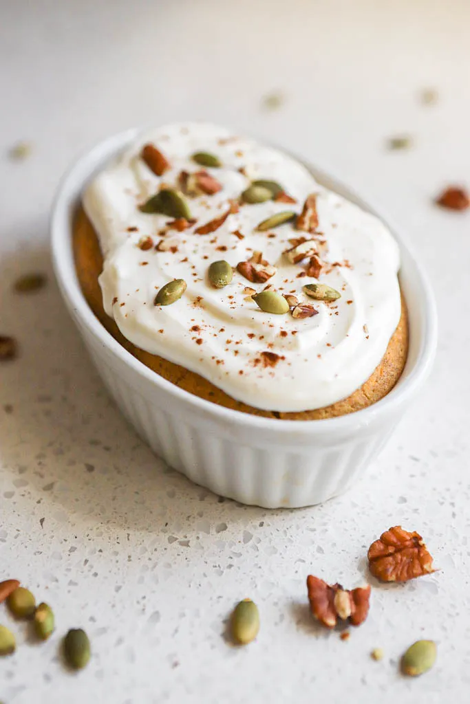 side shot of pumpkin baked oatmeal in white glass dish with sunflower seeds and walnuts