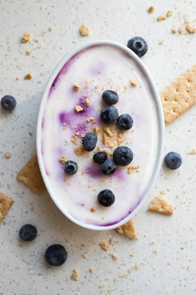 top down shot of blueberry cheesecake overnight oats with fresh fruit and graham crackers