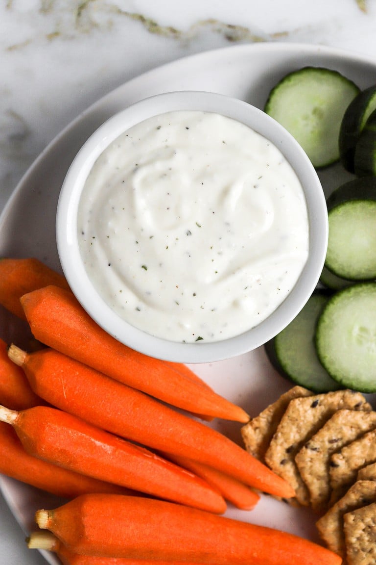 close up shot of raw carrots and cucumbers beside cottage cheese ranch dip in small bowl