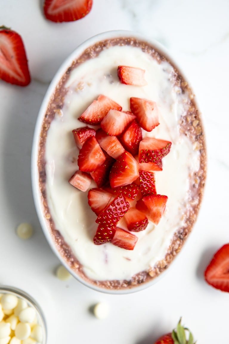 top down view of strawberry vanilla protein powder oats in a white ramekin with fresh strawberries chopped on top