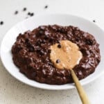 Brownie batter oatmeal in a white bowl with a dollop of peanut butter