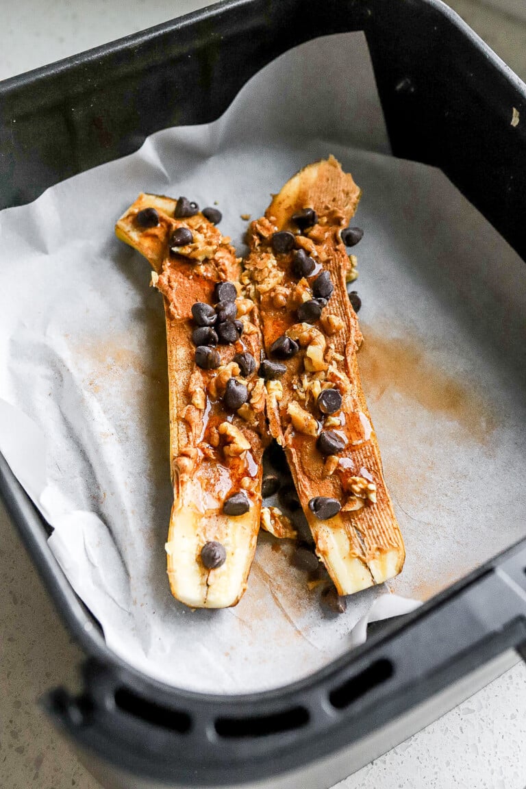 Side angle of a banana split into 2 in air fryer with chocolate chips, cinnamon, and peanut butter.