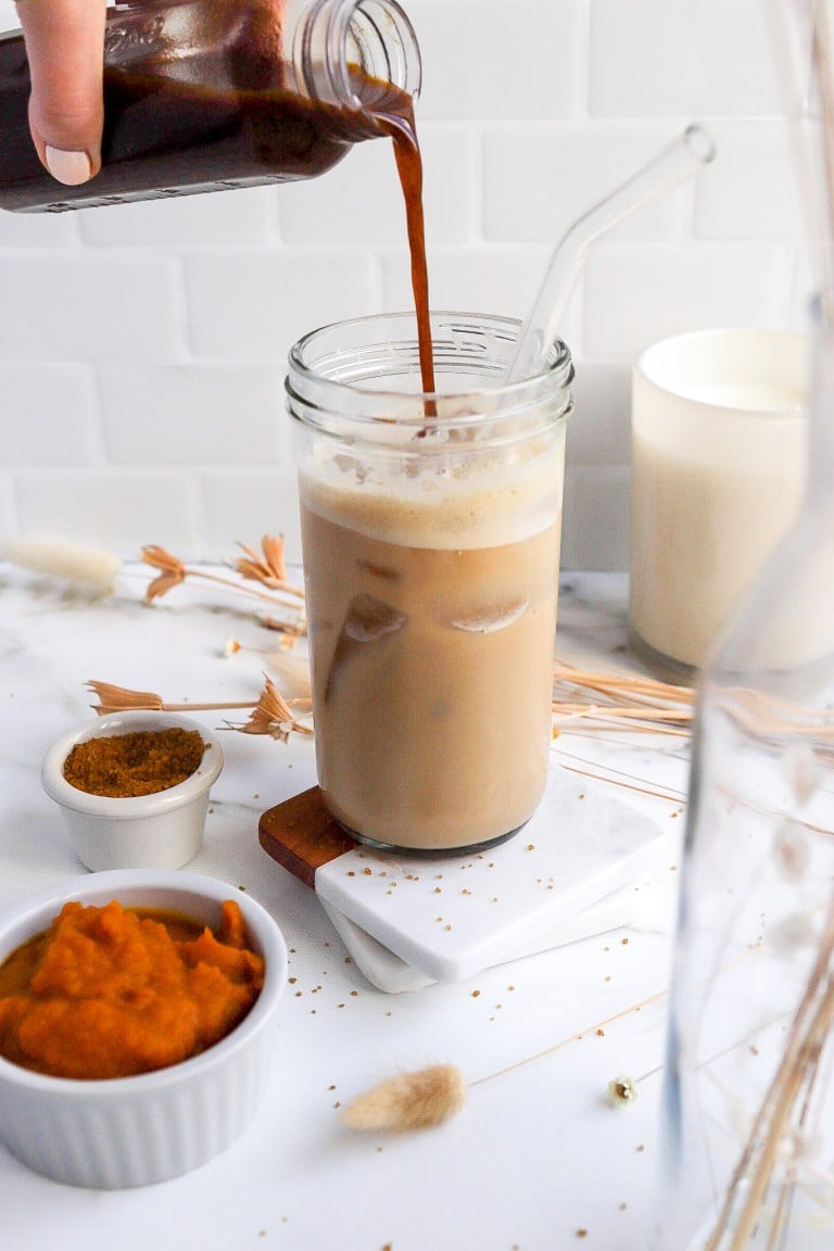 side angle of homemade pumpkin spice syrup being poured into an iced coffee