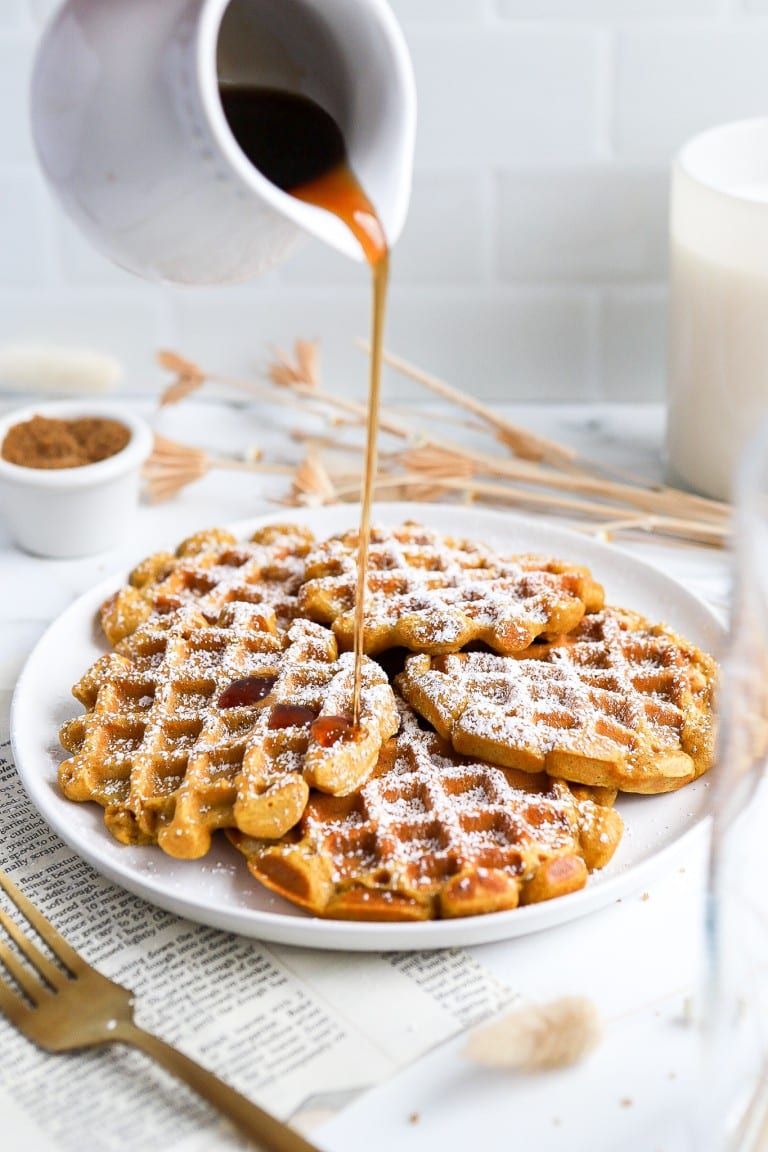 side angle of maple syrup being poured on pumpkin spice waffles