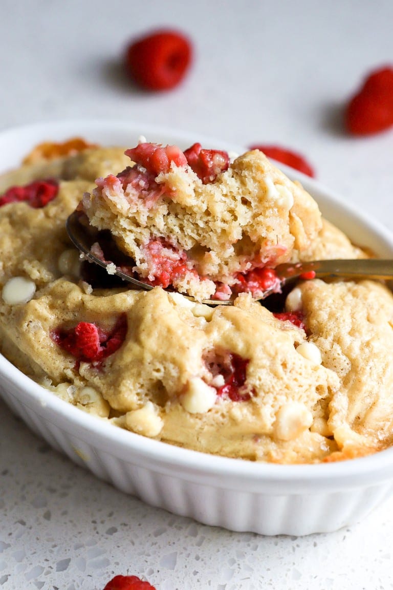 baked oatmeal recipe in white ramekin with fresh raspberries and gold spoon