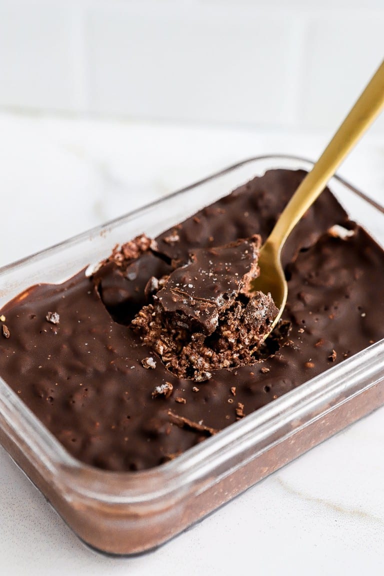 side angle of gold spoon going into glass container of chocolate crunch bar overnight oats