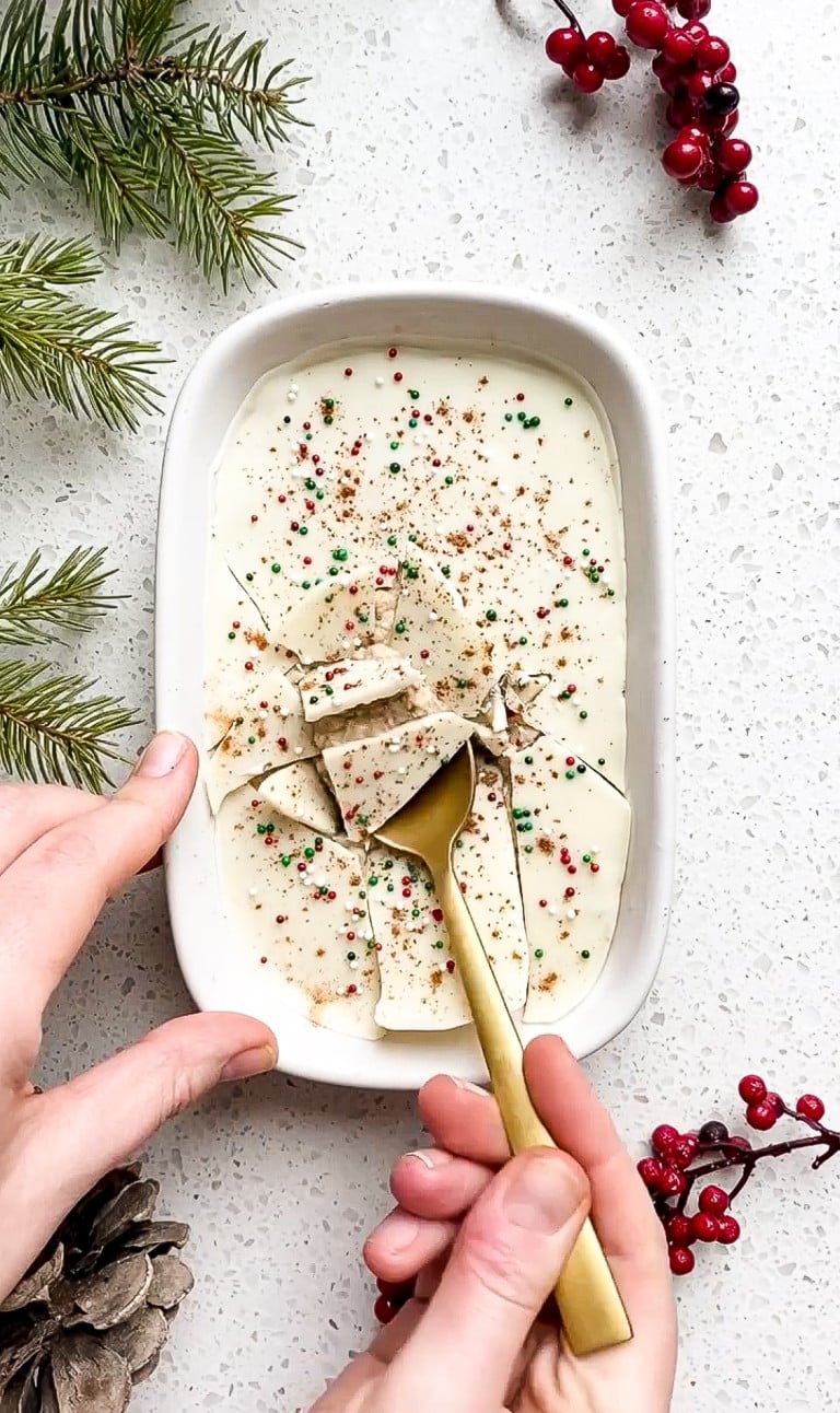 top down view of gold spoon cracking into eggnog oatmeal with green and red sprinkles