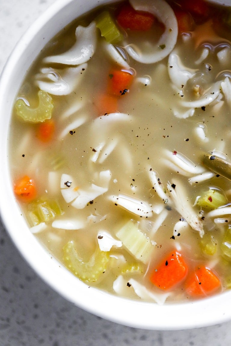 close up shot of homemade chicken carcass soup with egg noodles and carrots