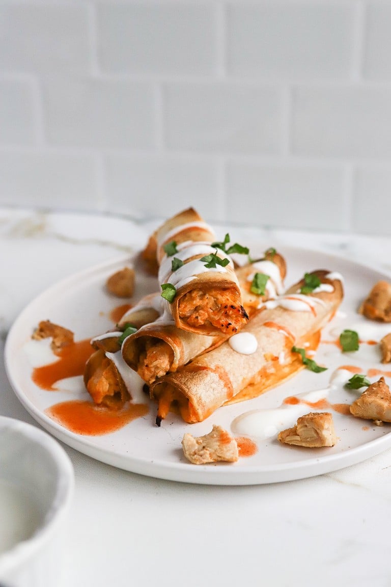 homemade taquitos fresh from the air fryer stacked on top of each other with ranch dressing and herbs