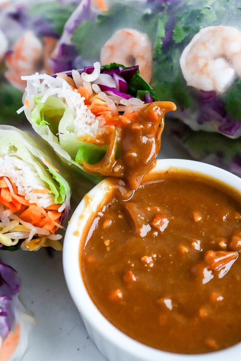 close up shot of rice paper rolls dipped into the small white bowl of creamy peanut sauce