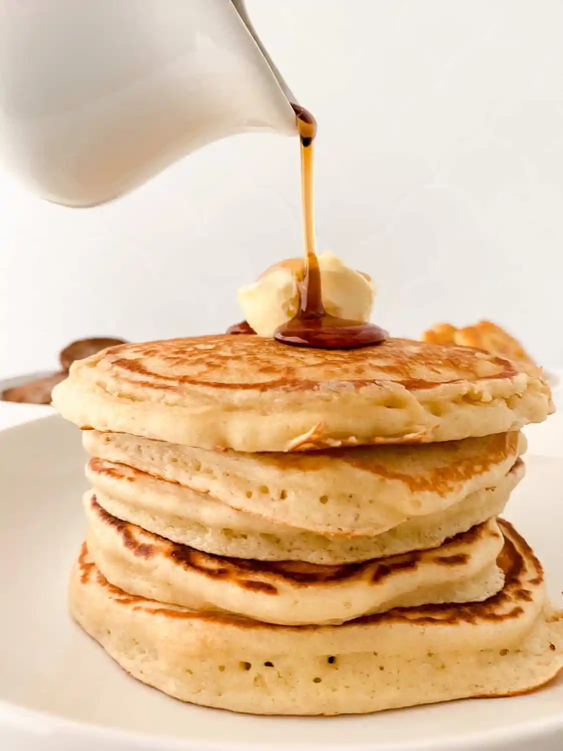 syrup being poured on stack of pancakes with butter on top