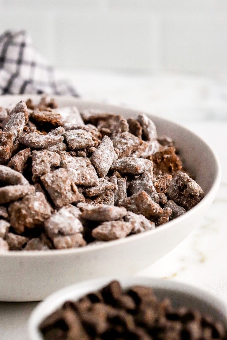 close up shot of muddy buddies in a bowl with white icing sugar coated on them