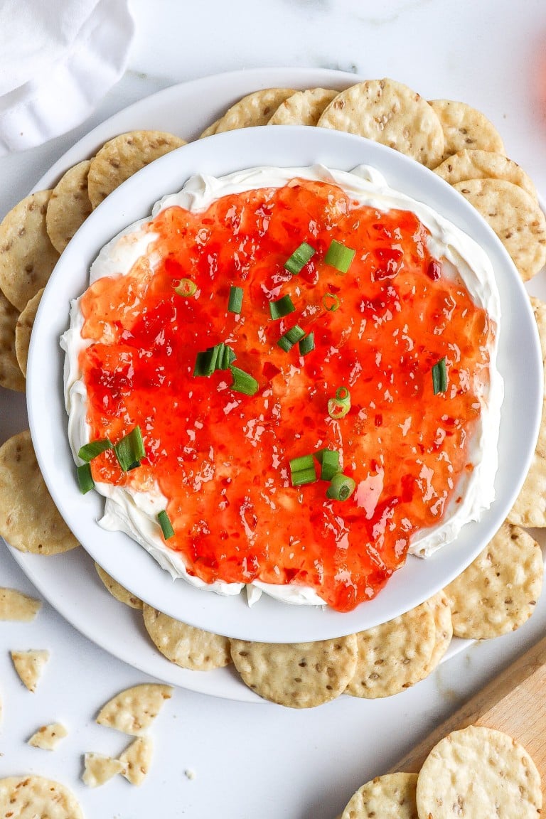 top down shot of red pepper jelly with cream cheese in a bowl with green onions on top