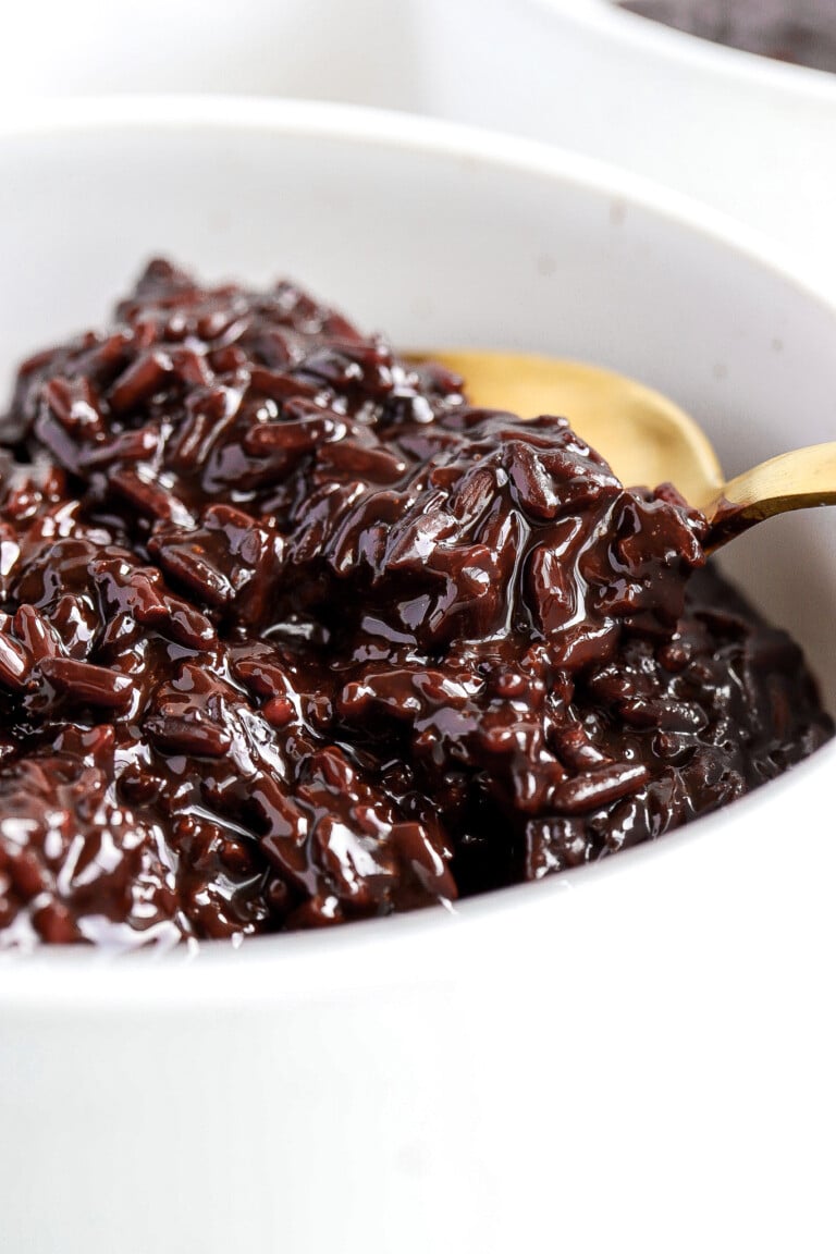 Close up shot of sweet chocolate rice porridge in small white bowl with gold spoon.