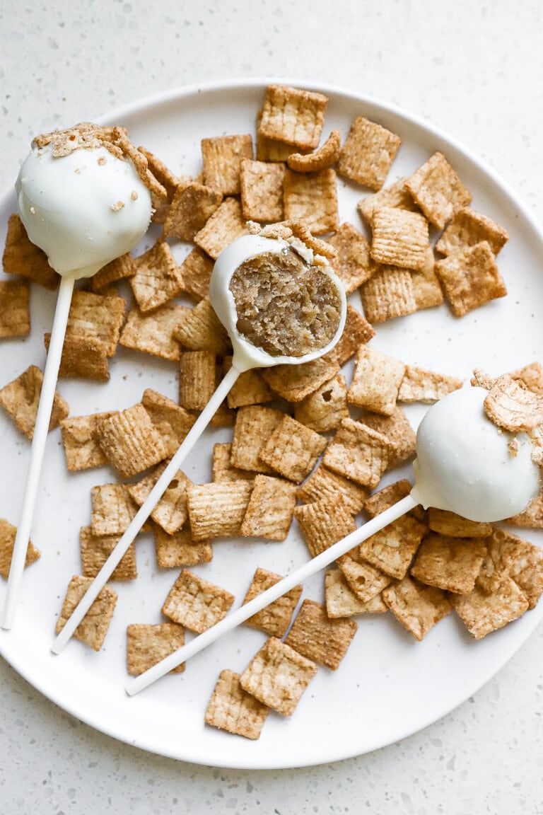 Top down view of easy Cinnamon Toast Crunch cake pops on white plate with cereal scattered around it.