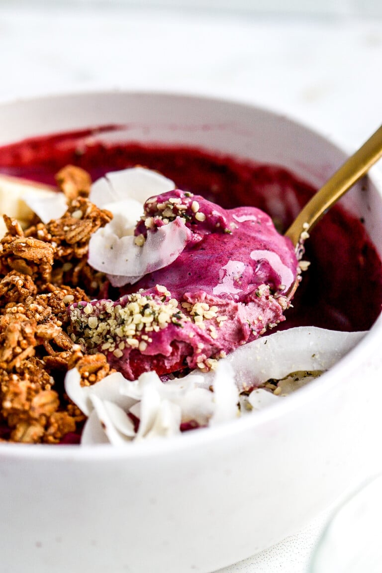 Side angle of smoothie bowl breakfast bowl with delicious toppings with gold spoon.