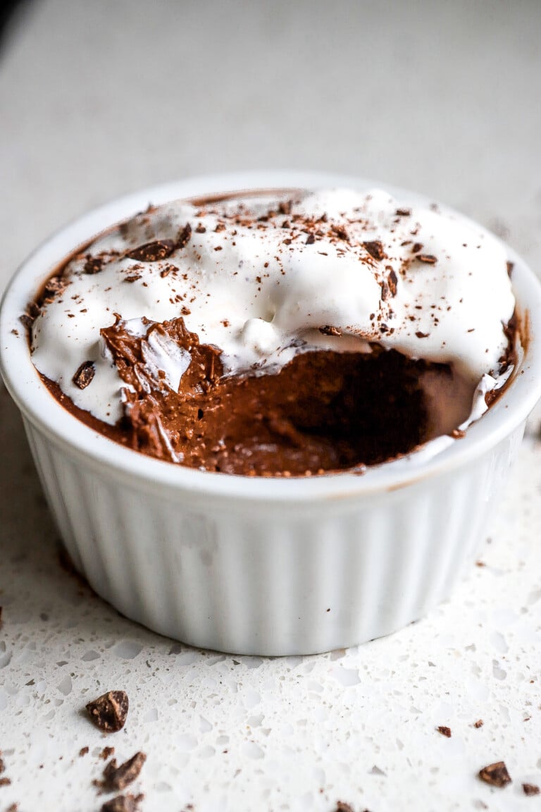 Side view of white ramekin full of chocolate protein pudding with whip cream and dark chocolate shavings.