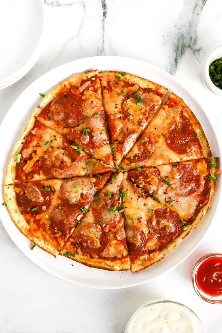 Top down view of easy cottage cheese pizza flatbread on white plate with pepperoni and green chives.