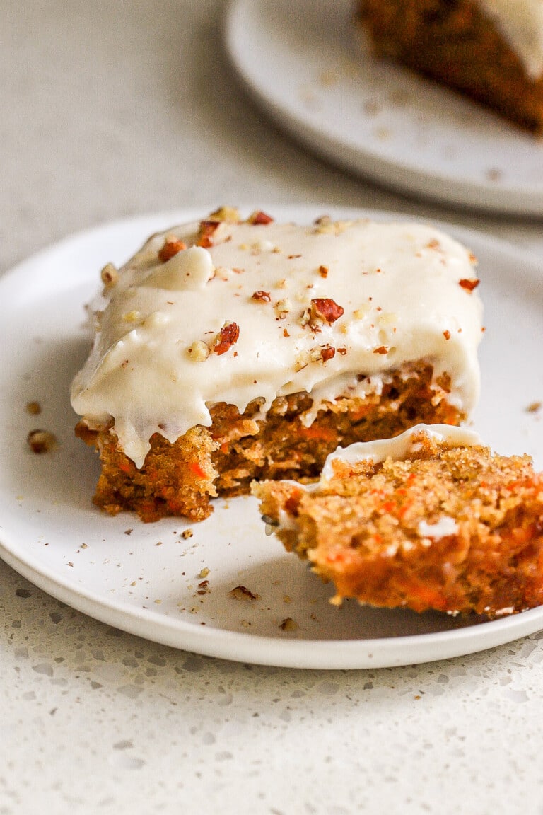 Side view of moist carrot sheet cake with cream cheese icing on small white plate.