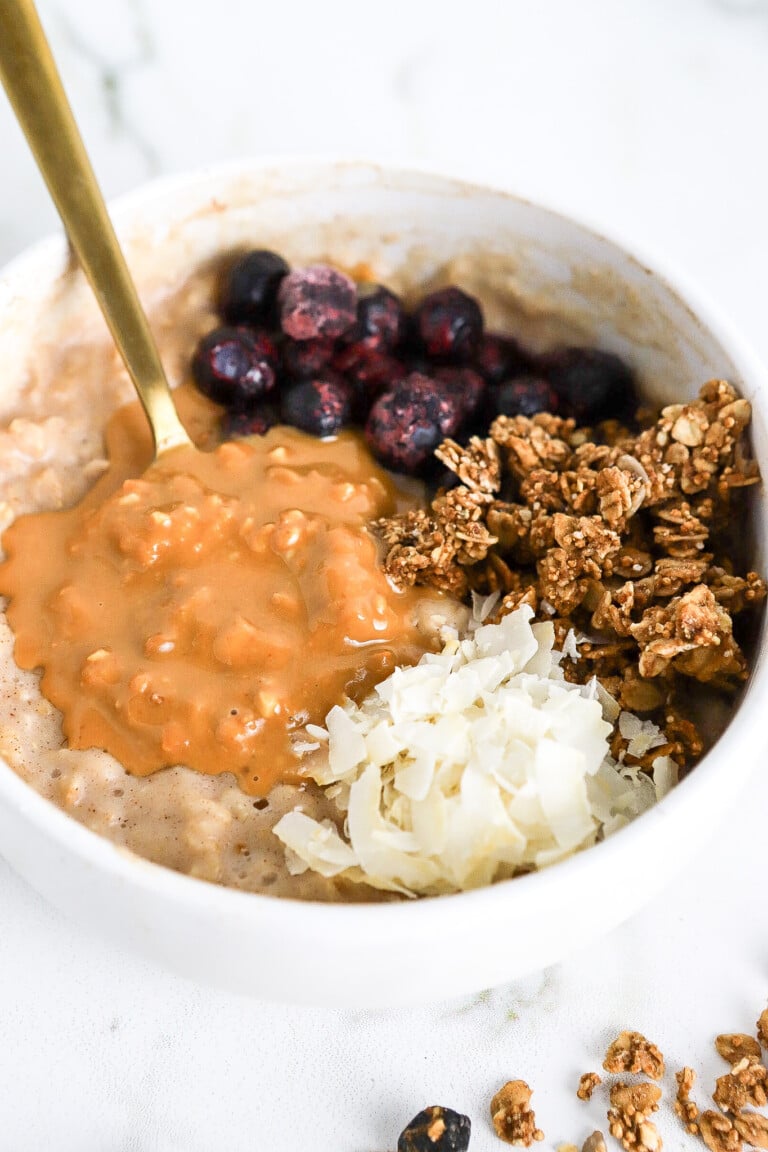 Side view of protein egg white oatmeal in white bowl with creamy peanut butter and blueberries.