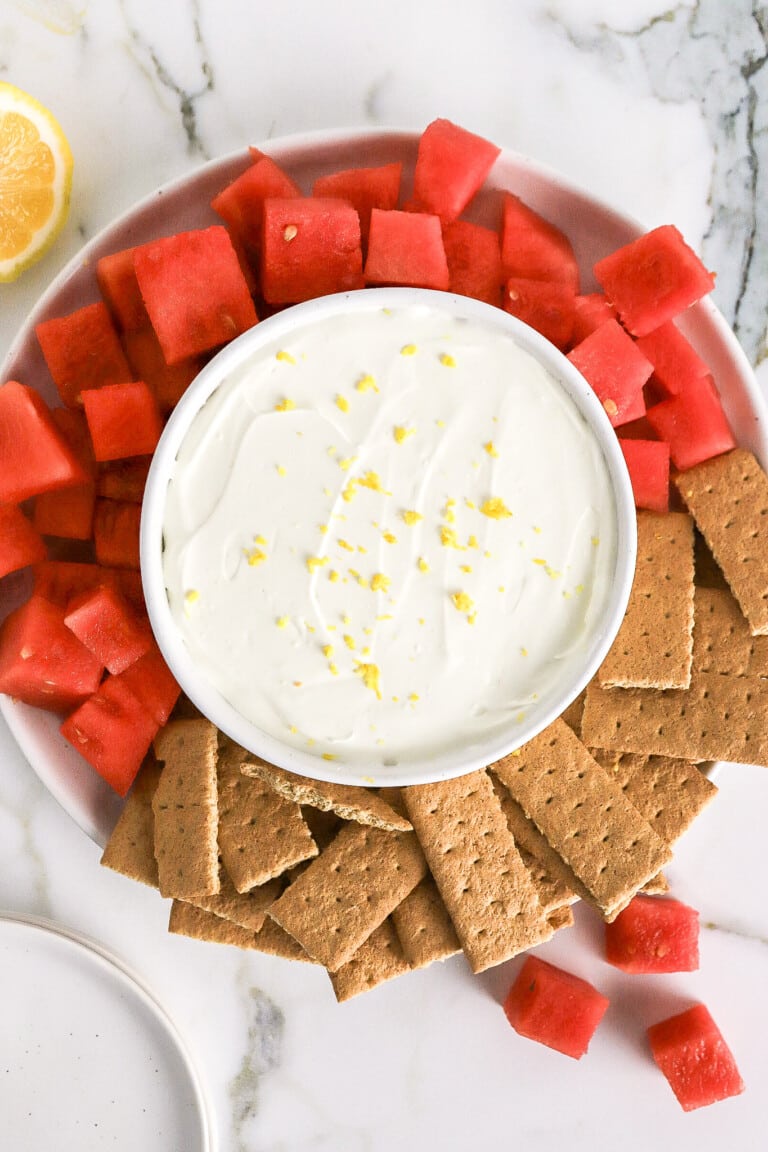 Top down view of protein fruit dip in small white bowl with watermelon and graham crackers around the dip.