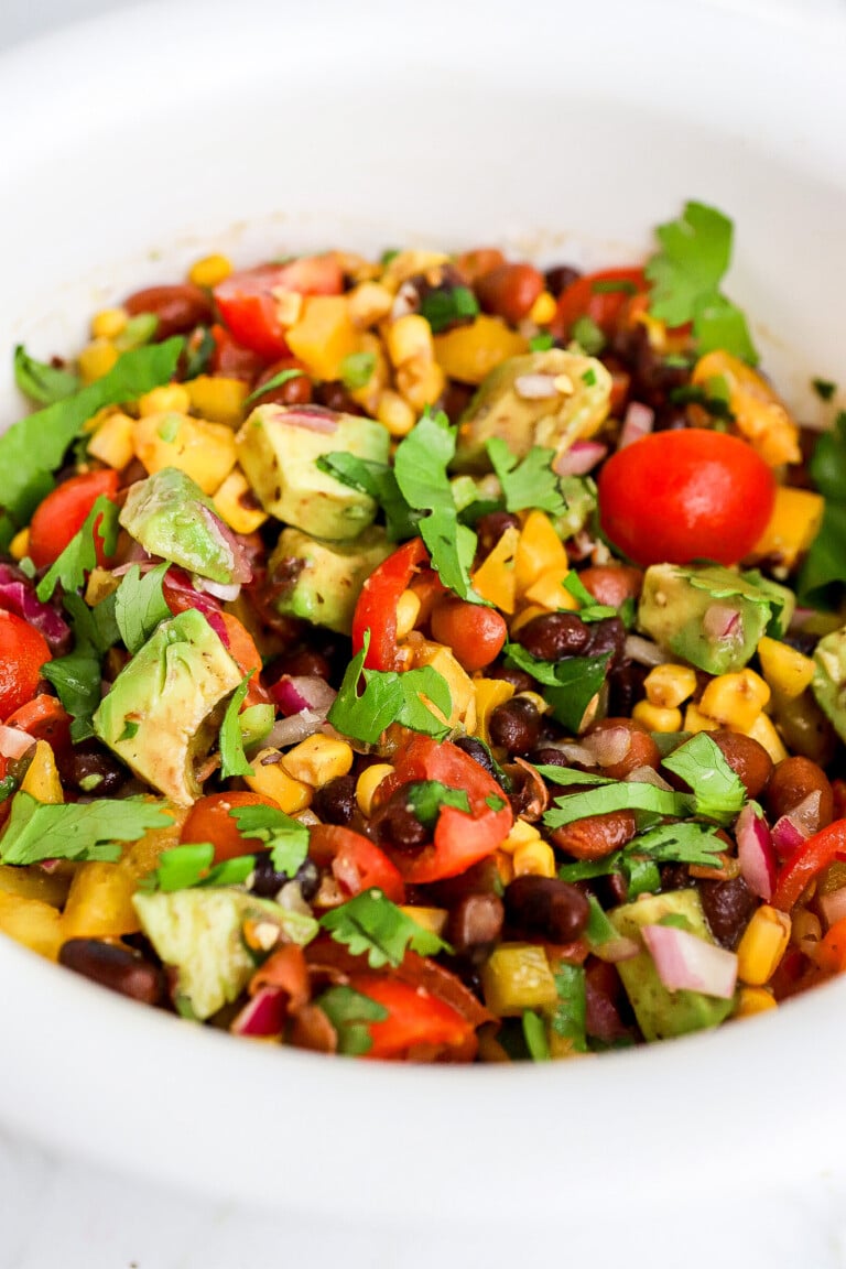 Side view of colourful cowboy caviar recipe in white bowl with fresh cilantro.