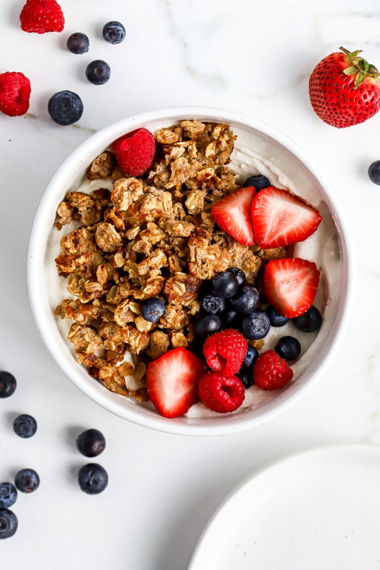 Top down view of a white bowl full of plain greek yogurt, fresh berries, and scrambled oats with berries scattered around the bowl.