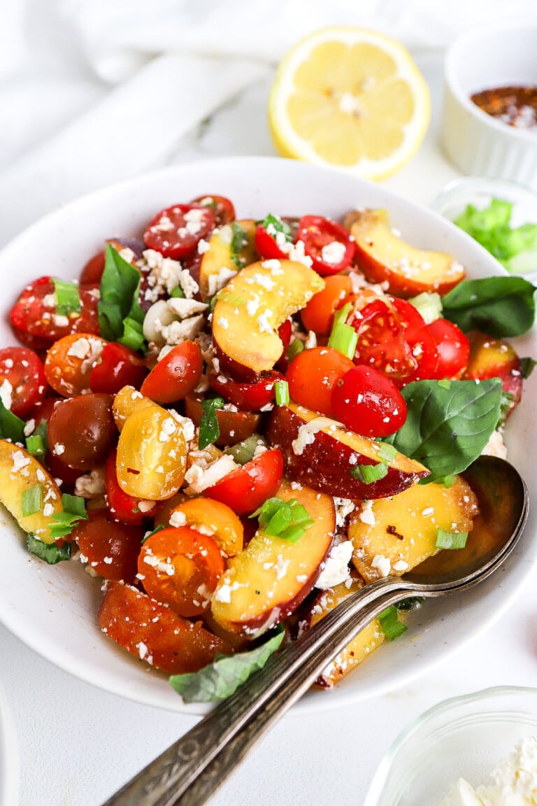 Close up shot of peach tomato feta salad with fresh basil leaves.