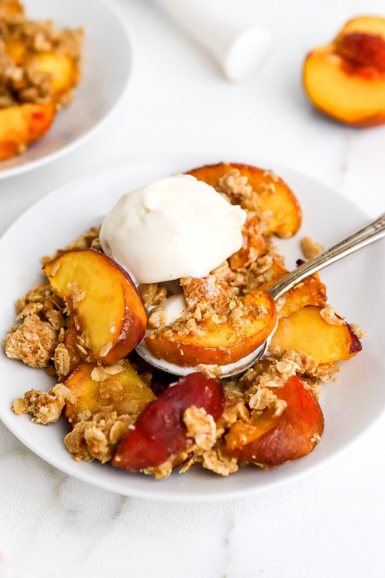 Side angle of air fryer peach crisp with a scoop of ice cream.