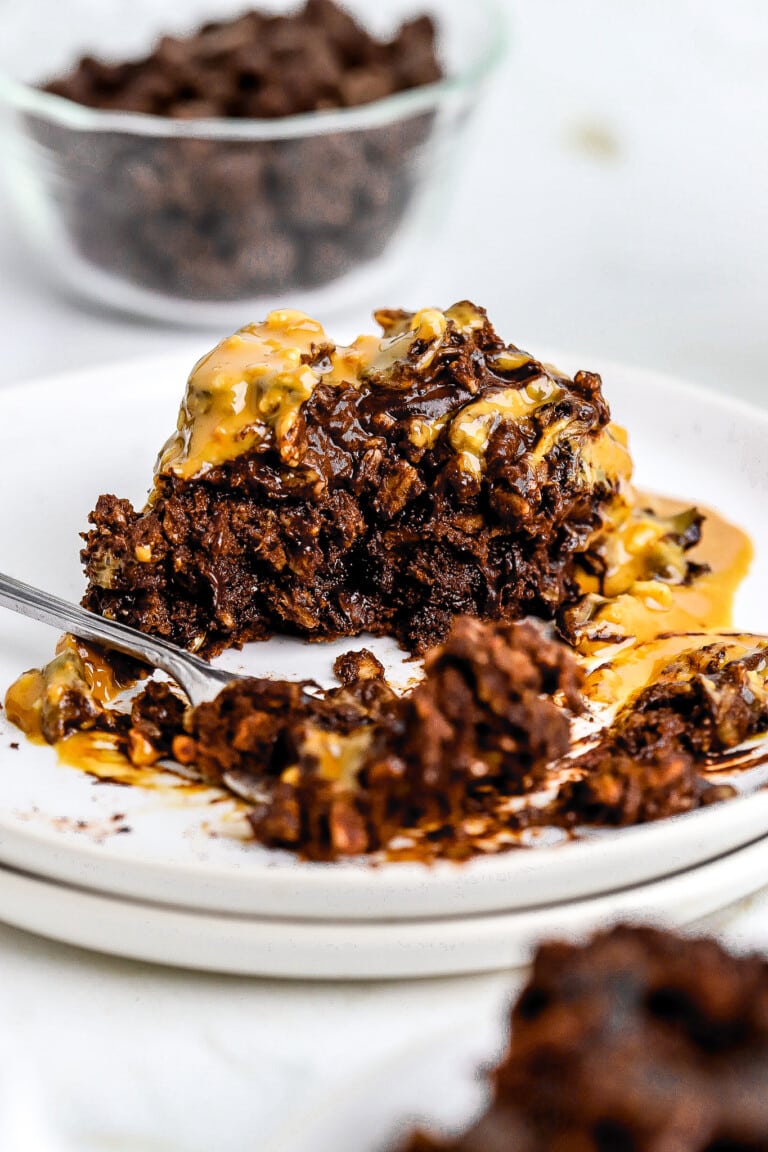 Front view of chocolate baked oatmeal on small white plate covered in peanut butter with a silver fork.