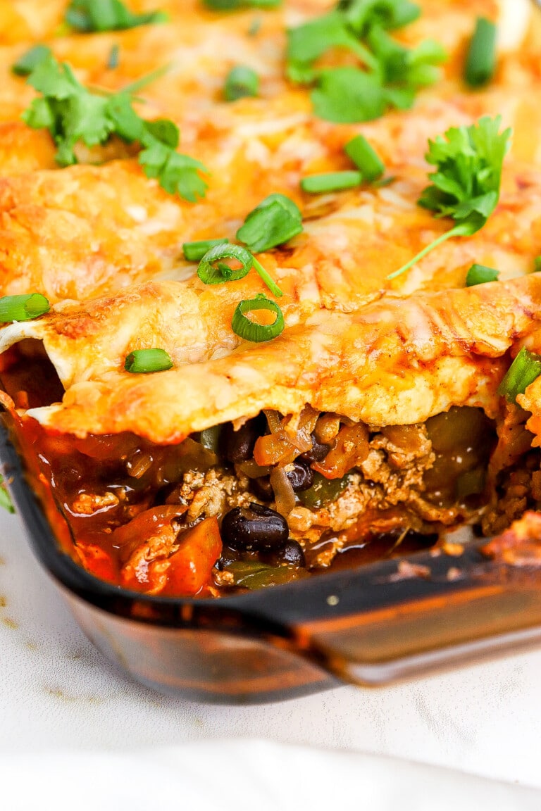 Close up view of a delicious ground turkey enchilada casserole with green onions and cilantro on top.