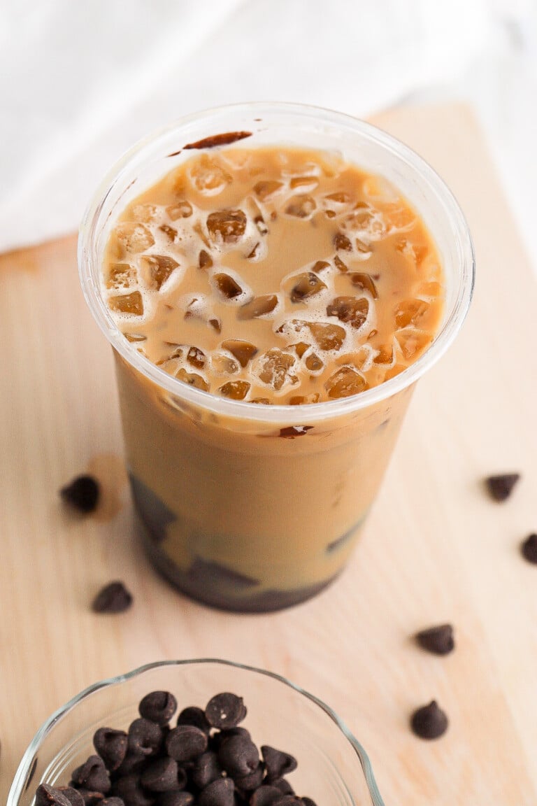 Close up view of an iced coffee in a plastic cup with chocolate chips on the countertop.