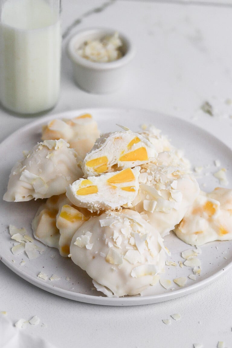 Side angle of mango yogurt clusters with glass of milk and coconut in background.