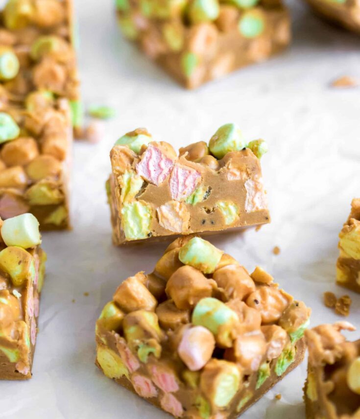 Close up view of peanut butter marshmallow squares with coloured marshmallows on parchment paper.
