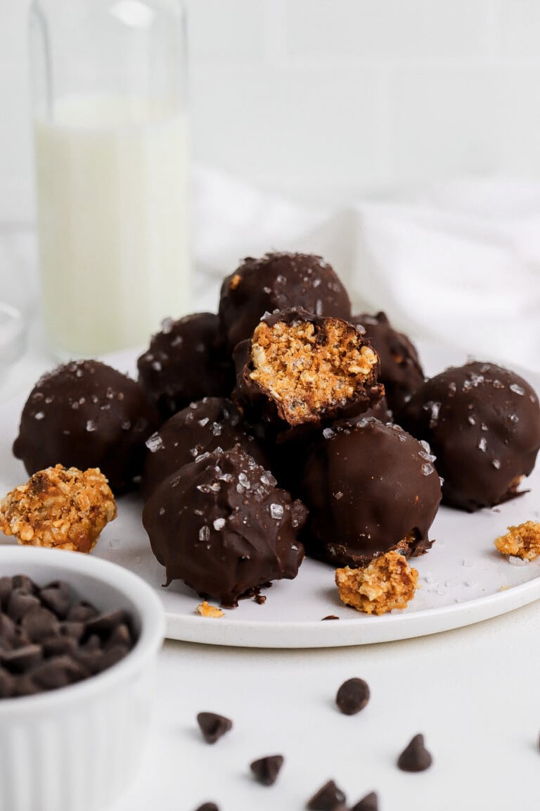 Side angle of peanut butter crunch balls on small white plate with chocolate chips in foreground.