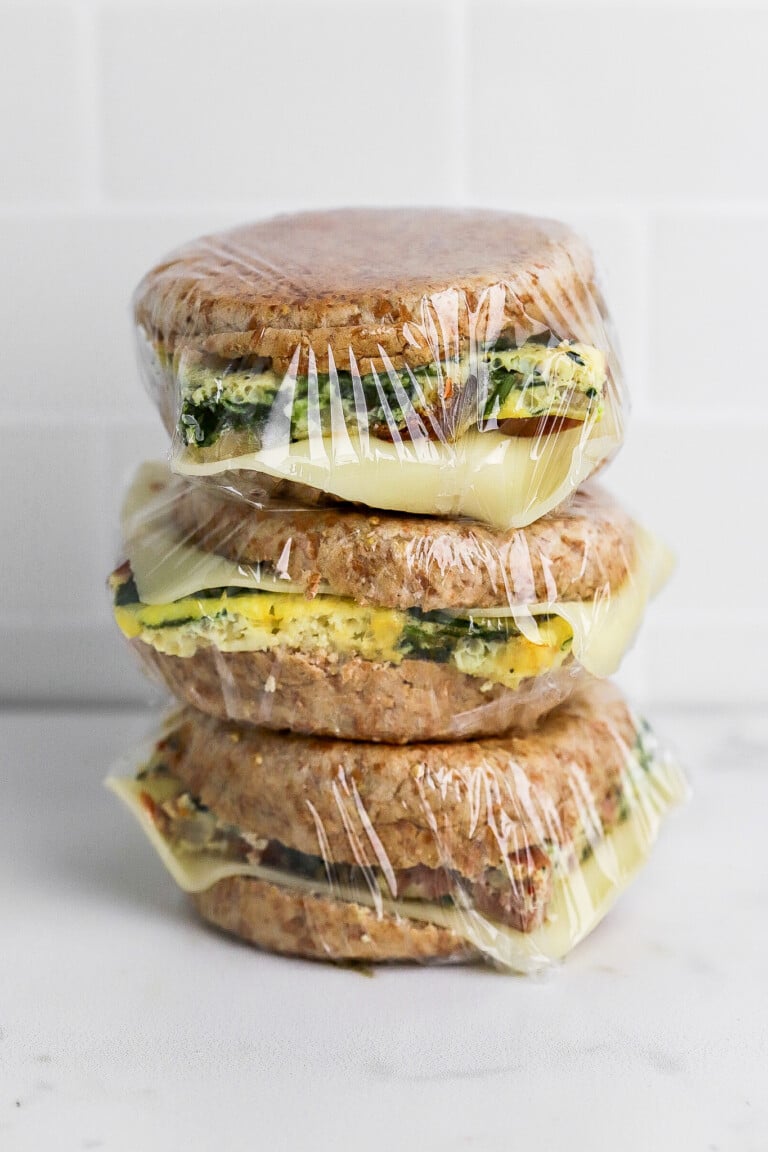 Side view of make ahead breakfast sandwiches wrapped in plastic wrap stacked on top of each other.