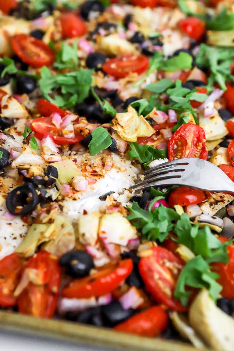 Close up shot of Mediterranean baked fish recipe on baking sheet with a bunch of fresh vegetables.