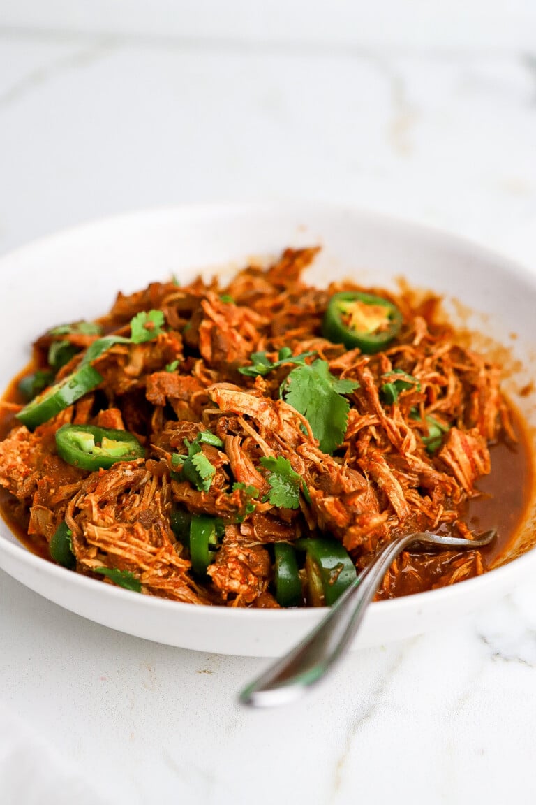 Front facing view of shredded chicken in white bowl with jalapeños and cilantro.