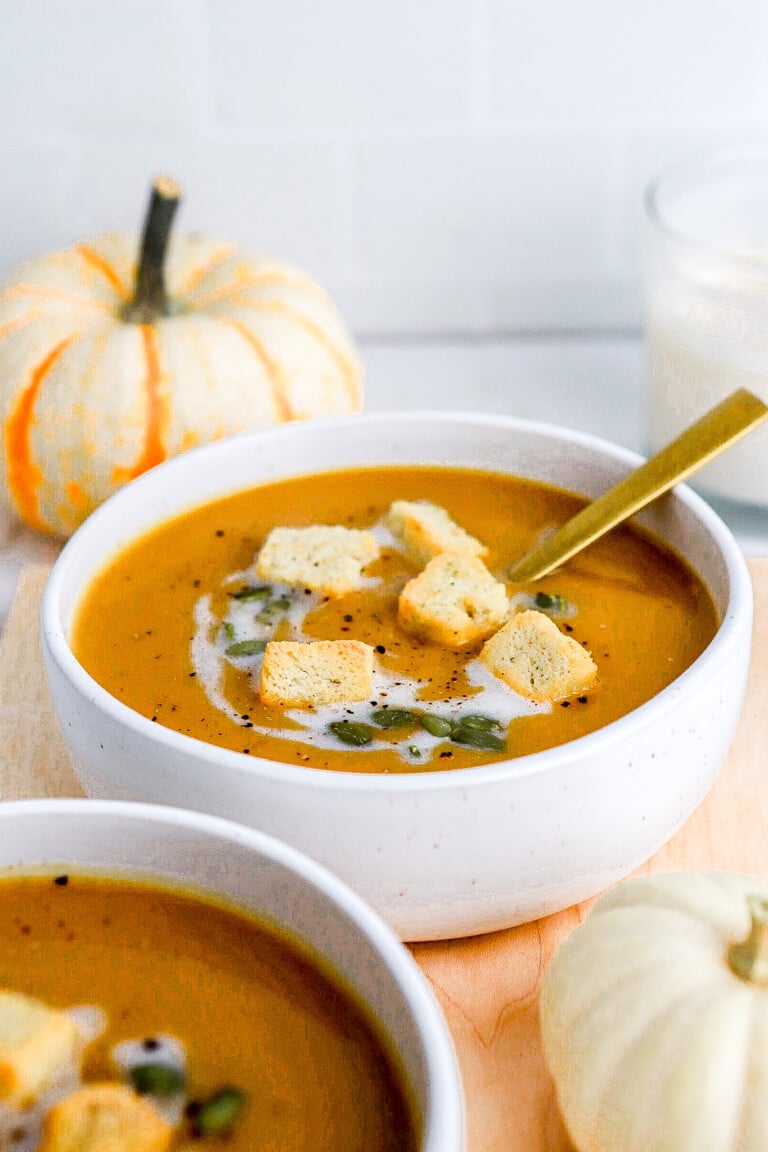 Side angle of soup with croutons in small white bowl with gold spoon.