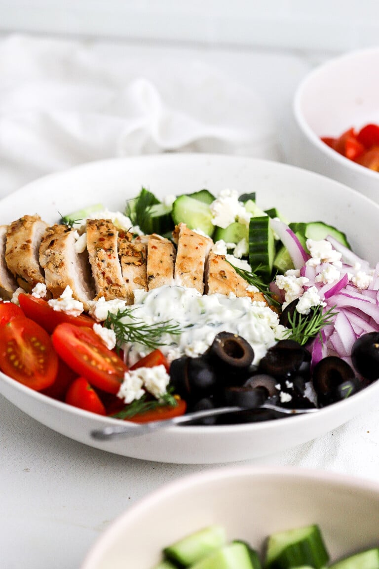 Side view of an easy greek chicken bowl with fresh cucumbers, cherry tomatoes, olives and red onion.